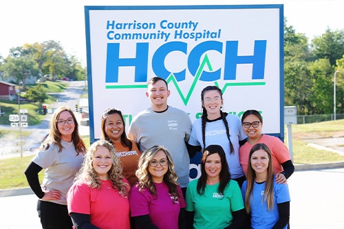A group of HCCH physical therapists in front of the hospital sign