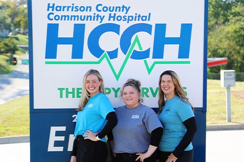 Three HCCH speech therapists in front of the hospital sign