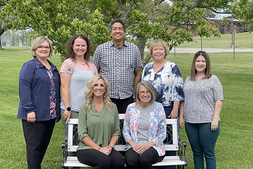 The HCCH Senior Life Solutions team posing for a photo around a bench on a sunny day