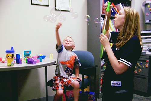 A therapists and a child playing with bubbles as a part of treatment